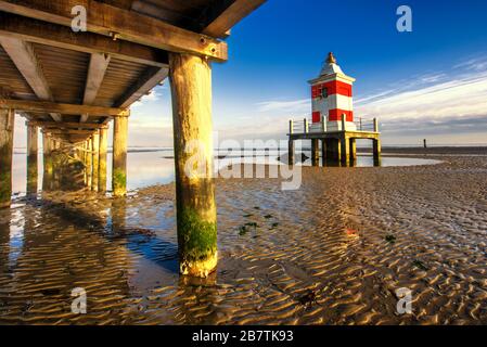 Pier und Leuchtturm bei Sonnenuntergang und Ebbe. Lignano Sabbiadoro, Provinz Udine, Friuli Julisch Venetien, Italien. Adriatische Meereslandschaft. Stockfoto