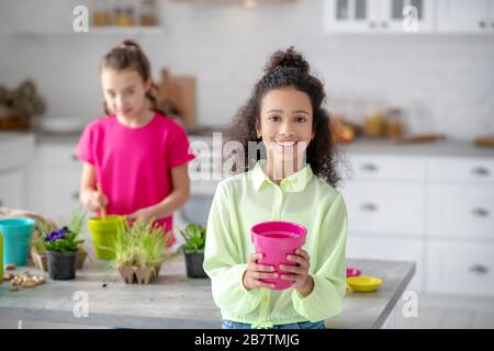 Lächelndes afroamerikanisches Mädchen, das einen Topf in ihren Händen hält Stockfoto