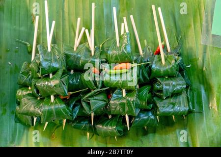 Khao tom, traditionelles thailändisches und laotisches Dessert, das aus gewürztem, gedämpftem, klebrigem Reis besteht, der in Bananenblätter eingewickelt ist Stockfoto