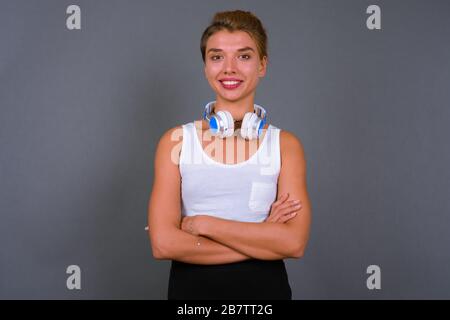 Junge schöne Geschäftsfrau mit blondem Haar, die Kopfhörer vor grauem Hintergrund trägt Stockfoto