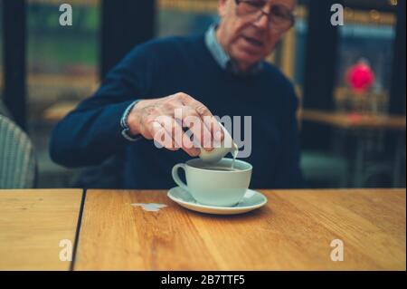Ein reifer Mann in einem Café schüttet Milch in seinen Kaffee und schüttet ihn auf den Tisch Stockfoto
