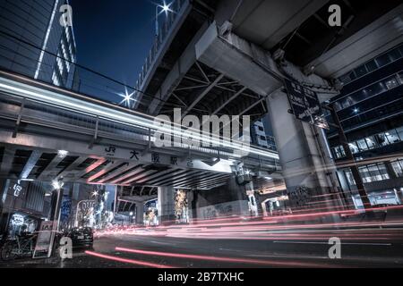 Blick auf die Nacht und einen Zug, der sich unter einer erhöhten Autobahn in Osaka, Japan, bewegt. Stockfoto