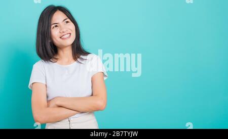 Portrait Asian Beautiful Happy Young Woman Smile tragen weißes T-Shirt, das mit einer Brust steht, die auf einem blauen Hintergrund nach oben blickt Stockfoto