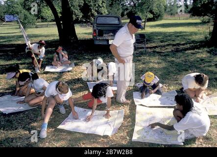 Bandera, Texas, USA, um 1991: Mädchen der vierten Klasse verwenden Kompass und Karte, um ihren Standort während eines nächtlichen Campingausflugs zu schätzen, während die Erwachsene Begleitperson nachschaut. ©Bob Daemmrich Stockfoto