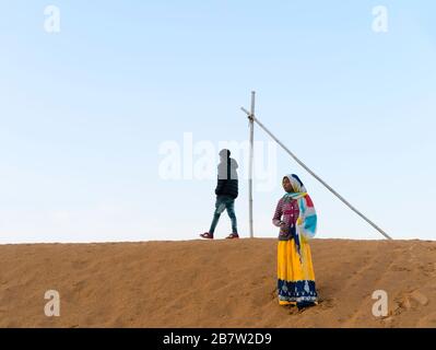 Junge Zigeunerfrau in traditioneller bunter Kleidung, die im Morgengrauen in der Wüste Thar bei Puschkar, Rajasthan, Indien, spazieren geht. Stockfoto