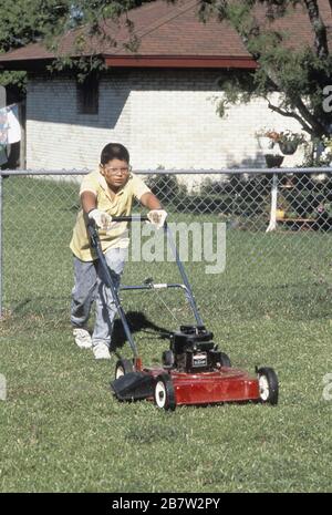 Austin, Texas USA,1988: Hispanischer Junge, 13, Rasenmähen mit gasbetriebenem Mäher. MR RR-0092. ©Bob Daemmrich Stockfoto