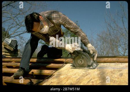 Volunteer verwendet Kreissäge, um Reparaturen auf dem Dach des einkommensschwachen Hausbesitzers vorzunehmen. HERR ©Bob Daemmrich Stockfoto