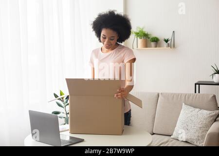 Lächelnde afroamerikanische Frau, in der Nähe von Box und Laptop Stockfoto