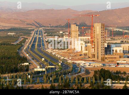 Entwicklung der Stadt Aschgabat in Turkmenistan. Lange mehrspurige Autobahn und Berge sichtbar. Neue Regierungsgebäude im Bau. Stockfoto