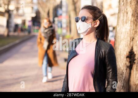 Schuss einer jungen Frau, die beim Ausbruch des Coronavirus auf der Straße eine Atemschutzmaske zum Schutz der Gesundheit trägt. Stockfoto