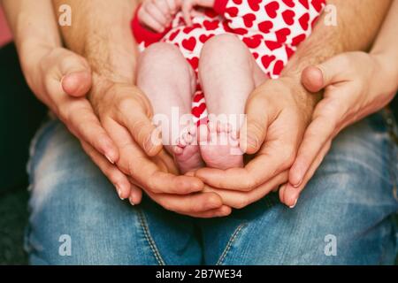 Füße eines neugeborenen Babys in den Händen der Eltern. Happy Family Konzept. Mutter und Papa umarmen die Beine ihres Babys Stockfoto