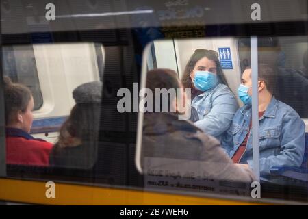 Die Menschen tragen an Bord eines U-Bahn-Zugs der Jubilee Line in London schützende Gesichtsmasken, da Pendler von zu Hause aus zu arbeiten wechseln und die Öffentlichkeit aufgefordert wird, sozialen Kontakt zu vermeiden, um die Ausbreitung von Coronavirus zu verhindern. Stockfoto