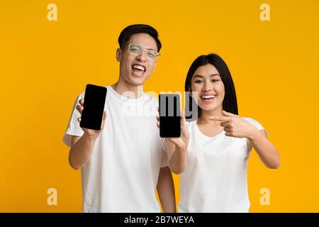 Lächelndes asiatisches Paar, das ihre Smartphones mit leeren Bildschirmen zeigt Stockfoto