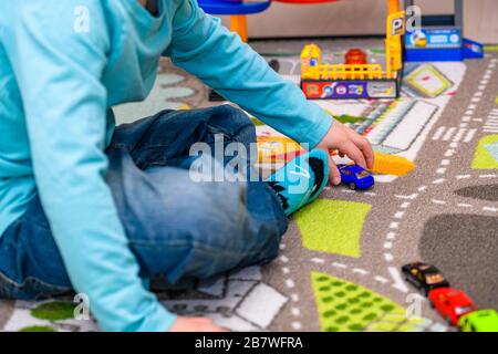 Fünf Jahre alter Junge, der auf einer Spielmatte mit Straßen Spielzeugautos spielt und auslegt. Der Junge ist mit einer blauen Jeans und einem türkisfarbenen Hemd bekleidet. Stockfoto