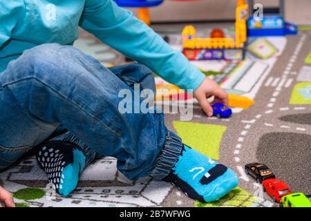 Fünf Jahre alter Junge, der auf einer Spielmatte mit Straßen Spielzeugautos spielt und auslegt. Der Junge ist mit einer blauen Jeans und einem türkisfarbenen Hemd bekleidet. Stockfoto