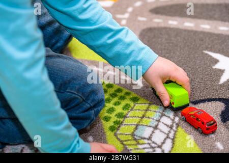 Fünf Jahre alter Junge, der auf einer Spielmatte mit Straßen Spielzeugautos spielt und auslegt. Der Junge ist in blaue Jeans gekleidet und hält einen Spielzeug-Krankenwagen. Stockfoto