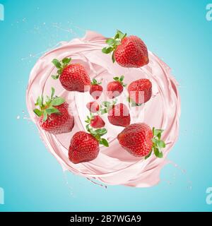 Erdbeer-Milchshake spritzt mit Früchten, auf blauem Grund Stockfoto