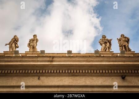 Detail der Säulenhallen am Petersplatz mit Statuen von Heiligen und dem Himmel im Hintergrund. Stockfoto