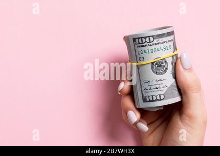 Blick von oben auf die weibliche Hand mit einem Pack von gewalzten Geld auf farbigen Hintergrund. Hundert Dollar. Business Konzept mit leeren Raum für Ihr Design. Stockfoto