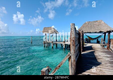 Alter Pier mit Blick auf das karibische Meer und im Hintergrund ein kleiner Palapa mit einem Touristen auf einer Hängematte. Reise- und Naturkonzept. Stockfoto