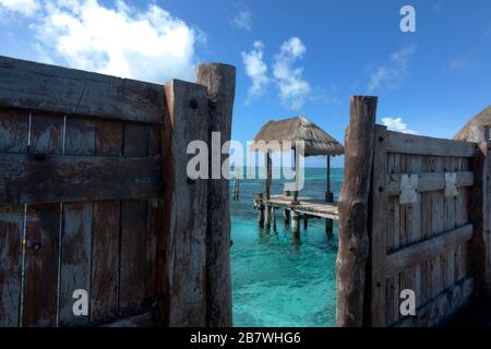 holztür an einem alten Pier mit Blick auf das karibische Meer und im Hintergrund ein kleines Palapa. Reise- und Naturkonzept. Stockfoto