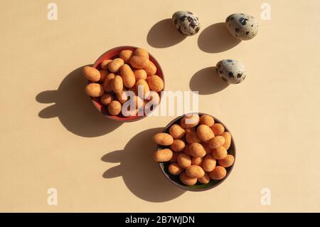 Drei Eier und zwei Schüsseln mit Nüssen mit Schatten wie Kaninchen auf gelbem Hintergrund. Modisches, konzeptionell minimalistisches Foto für den Osterurlaub 2020 Stockfoto