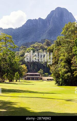 Blick auf die 18. Fahrrinne vom T-Shirt in Richtung Putting Green und das Clubhaus unter dem Berg Gunung Mat Cincang, dem Rainforest Golf Co Stockfoto