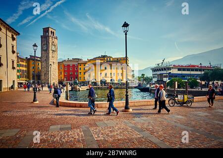 Riva del Garda, Lago di Garda, Italien - 13. Oktober 2019:Touristen, die einen Spaziergang am Gardasee genießen, bunter Herbst in Riva del Garda umgeben von einem Mund Stockfoto