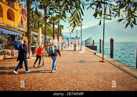 Riva del Garda, Lago di Garda, Italien - 13. Oktober 2019:Touristen, die einen Spaziergang am Gardasee genießen, bunter Herbst in Riva del Garda umgeben von einem Mund Stockfoto