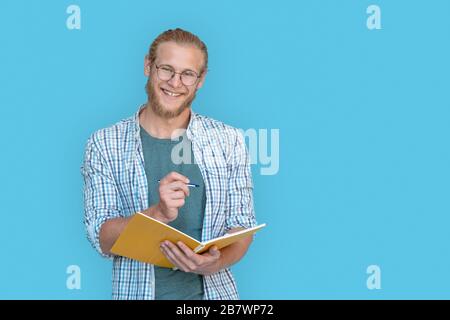 Happy man Student Hold Schreiben in Notizbuch isoliert auf blauem Hintergrund, Porträt. Stockfoto