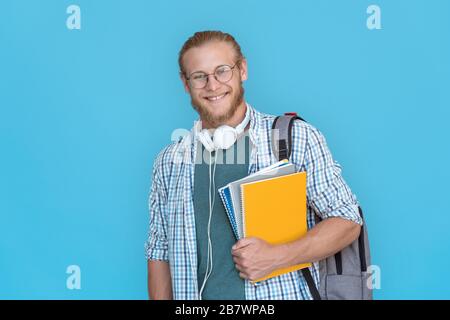 Happy man Student hält Rucksackworkbücher isoliert auf blauem Hintergrund. Stockfoto
