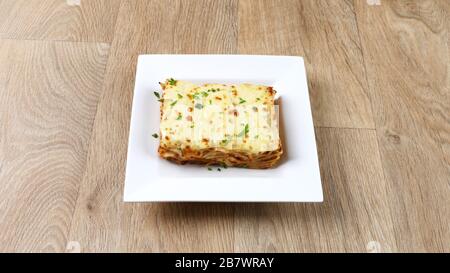 Klassische lasagna-bolognesische Portion isoliert serviert auf einer weißen Platte auf Holztischhintergrund Stockfoto