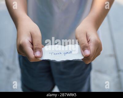 Der Junge, der ein Stück Papier mit dem Wort hält, dankt Ihnen in der Handfläche, die glücklicher ist. Stockfoto