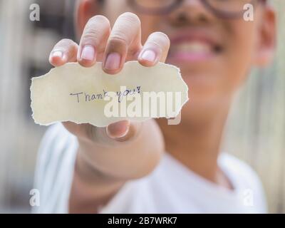 Der Junge, der ein Stück Papier mit dem Wort hält, dankt Ihnen in der Handfläche, die glücklicher ist. Stockfoto