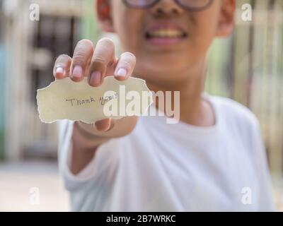 Der Junge, der ein Stück Papier mit dem Wort hält, dankt Ihnen in der Handfläche, die glücklicher ist. Stockfoto