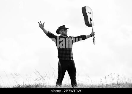 Inspiriert land Musiker. Landhausstil. Sommer Urlaub. Wandern Song. United mit der Natur. Stattlicher Mann mit Gitarre. Country Music Konzept. Gitarrist Land Sänger stand im Feld Himmel Hintergrund. Stockfoto