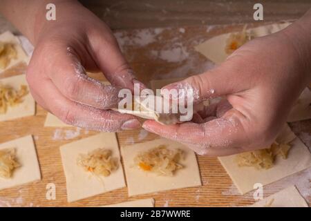 Eine Frau sculpt Knödel und Ravioli aus Kneten und Kohl. Sperrholzschneidplatte, Holzmehlsieb und Walzstift aus Holz - Werkzeuge für Stockfoto