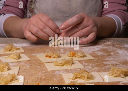 Eine Frau sculpt Knödel und Ravioli aus Kneten und Kohl. Sperrholzschneidplatte, Holzmehlsieb und Walzstift aus Holz - Werkzeuge für Stockfoto