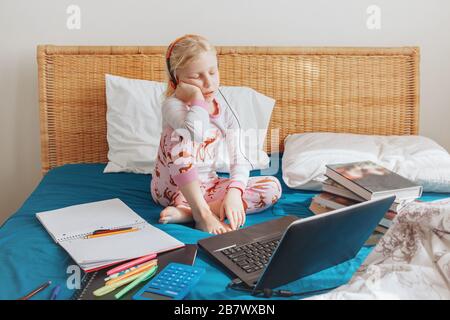 Müde gelangweilte kaukasische Mädchen im Bett sitzen Lernen online im Internet. Virtuelle Unterrichtsstunde zum Video während der Selbstisolierung zu Hause. Entferntes remo Stockfoto