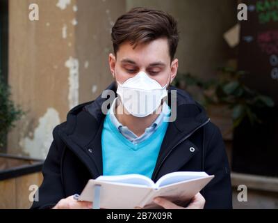 Besorgter Mann, der FFP3 Gesichtsschutzmaske in der Innenstadt trägt und regelmäßig mit seinem Telefon macht. Stockfoto