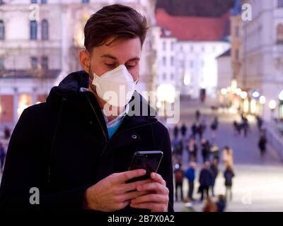 Besorgter Mann, der FFP3 Gesichtsschutzmaske in der Innenstadt trägt und regelmäßig mit seinem Telefon macht. Stockfoto