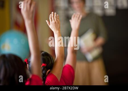 Schüler mit erhobenen Händen in einem Klassenzimmer. Stockfoto