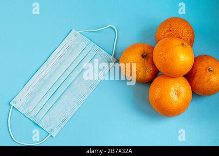 Eine sanitäre Maske verhindert den Eintritt des Corona-Virus oder anderer Krankheiten. In der Nähe liegen Früchte zur Heilung des Körpers. Vitamine auf blauem Hintergrund. Stockfoto