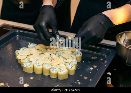 Weibliche Hände gießen Käse auf Cannelloni mit einer sanften Creme aus Ricotta und Spinat. Kochen Stockfoto