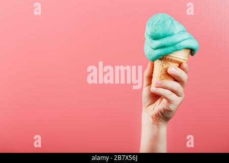 Eis in der Hand eines Kindes schmilzt auf einem rosafarbenen Hintergrund. Der Waffelkegel mit blauem Eis schmilzt. Stockfoto