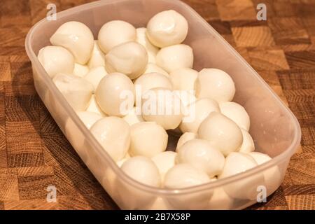 Mini-Mozzarella-Käsekugeln in einer Kunststoffplatte auf einem Holztisch. Zutat für Salat Stockfoto