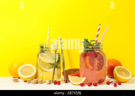 Glasgefäße mit Limonade und Zutaten vor gelbem Hintergrund. Frisches Getränk Stockfoto