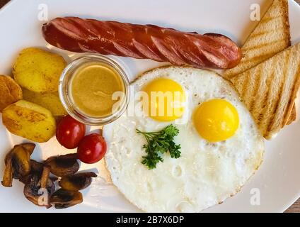 Traditionelles komplettes Frühstück mit Spiegeleiern, Wurst, Pilzen, gegrillten Tomaten und Kartoffelkeilen. Draufsicht Stockfoto