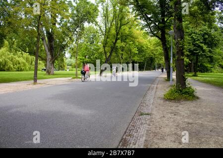 Blick auf Fahrradfahrer, Bäume und Straße im Vondelpark in Amsterdam. Es handelt sich um einen öffentlichen Stadtpark von 47 Hektar. Es ist ein Sommertag. Stockfoto