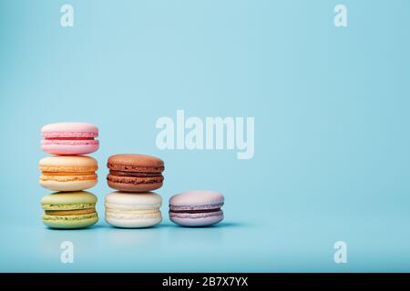 Makkaroni-Kekse verschiedener Farben sind in Form von Pyramidenstufen auf blauem Grund angeordnet. Stockfoto